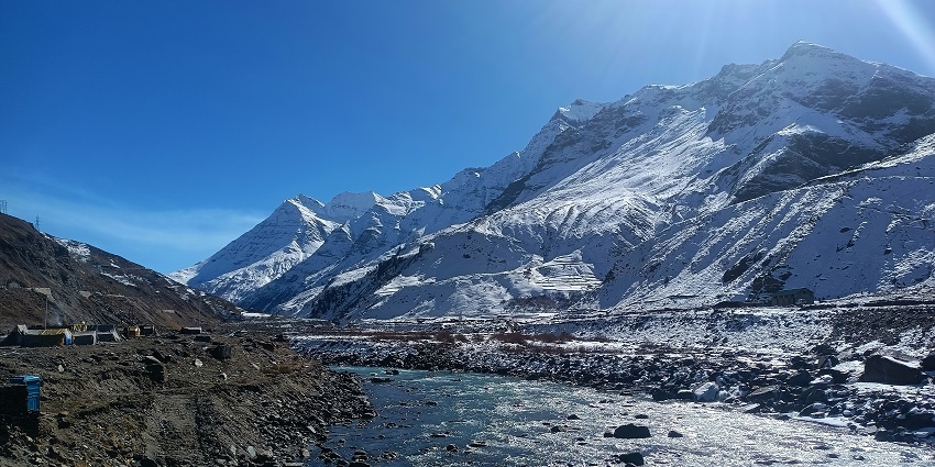 Snow-capped mountains and a clear river under a bright blue sky in Manali, Himachal Pradesh