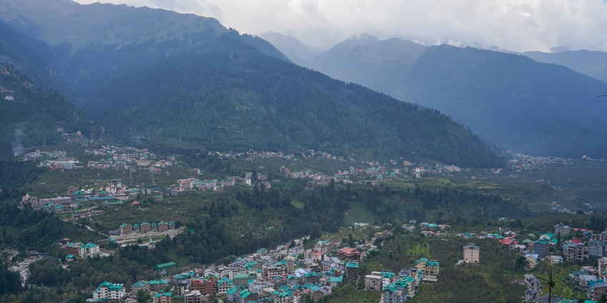 An aerial view of a hill city with lush greenery and mountains in the background
