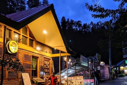 A breathtaking view of a brown hut in Manali with a man standing in front of it.