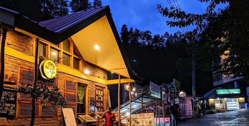 A breathtaking view of a brown hut in Manali with a man standing in front of it.