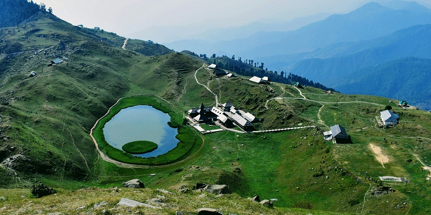 A breathtaking view of a lake in Mandi encircled by lush greenery and mountains.