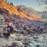 A breathtaking view of a river flowing through a Manikaran with houses on the side.