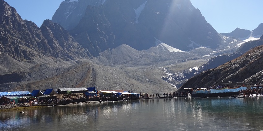 View of Manimahesh lake surrounded by snow-covered mountains during day time