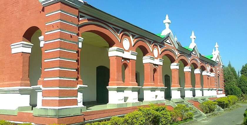 A frontal view of a red and white concrete building with lush greenery during the day.