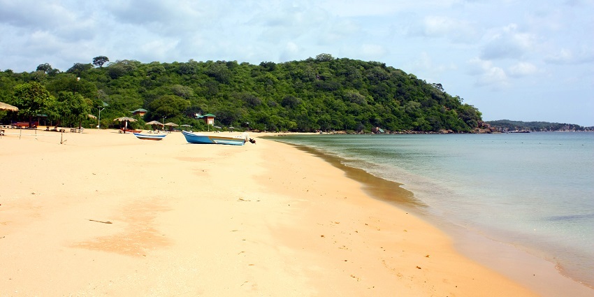 Marble Beach with smooth white pebbles, clear turquoise water, and rocky cliffs surrounding it.