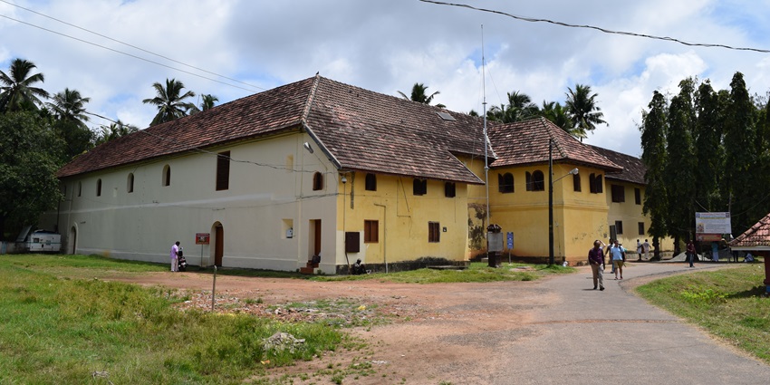 A historical palace built like a building with yellow walls and a hut-style roof, surrounded by trees