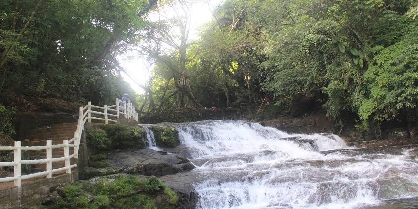 A breathtaking view of the Mawphlang Falls surrounded by thick lush green meadows.