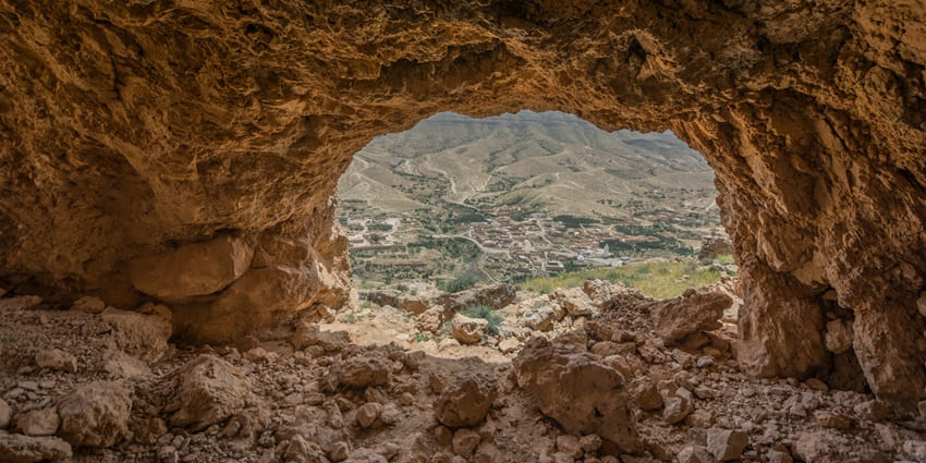 A picture of a beautiful cave from the inside with a hilly village visible in the background