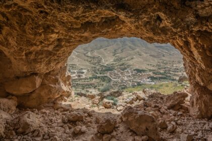 A picture of a cave system with a man standing at its opening around trees and greenery