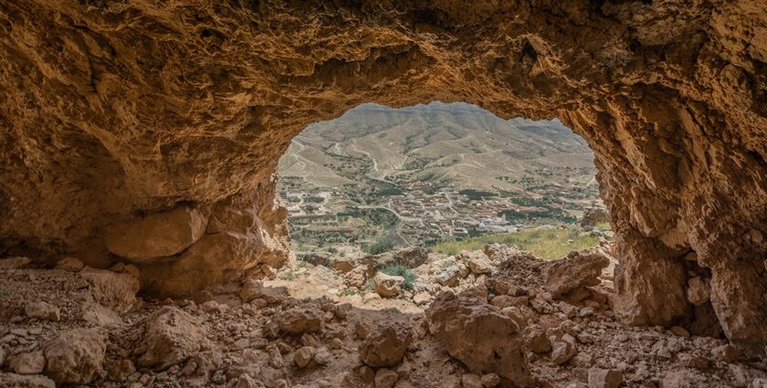 A picture of a cave system with a man standing at its opening around trees and greenery