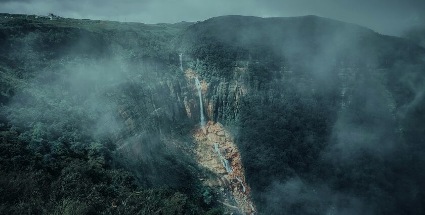 A mesmerising view of a waterfall in Meghalaya surrounded by lush greenery during the day.