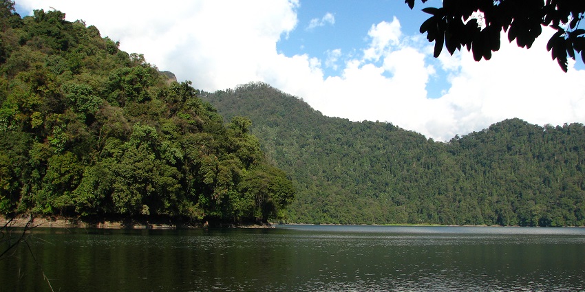 Serene water of the lake reflecting the forested shores and the mountains far ahead