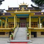 A stunning frontal view of a yellow and brown monastery around tall trees during the day.