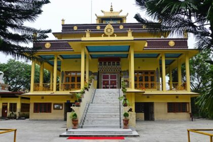 A stunning frontal view of a yellow and brown monastery around tall trees during the day.