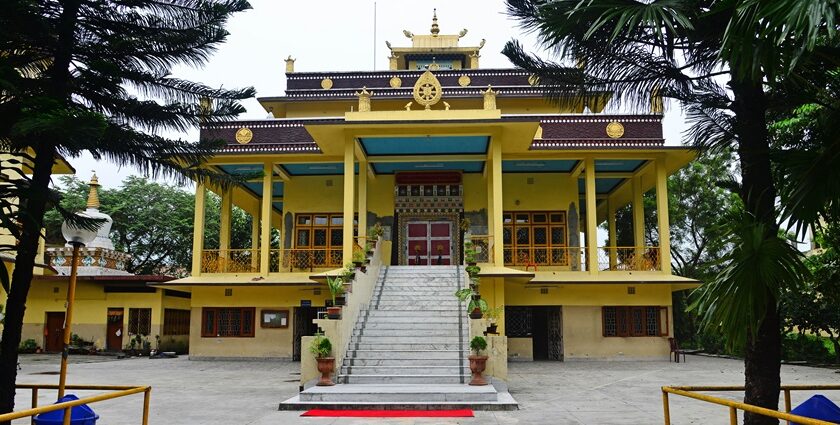 A stunning frontal view of a yellow and brown monastery around tall trees during the day.