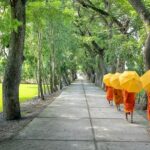 The monks walk on a pathway in the interiors of a monastery during the day.