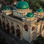 A breathtaking view of a mosque with green and white architecture with houses behind it.