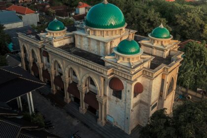 A breathtaking view of a mosque with green and white architecture with houses behind it.