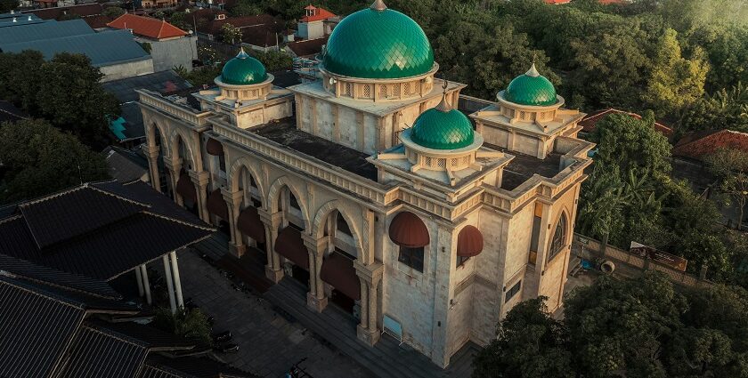 A breathtaking view of a mosque with green and white architecture with houses behind it.