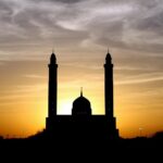 A silhouette of a mosque with a scenic backdrop of cloudy skies with a beautiful sunset.