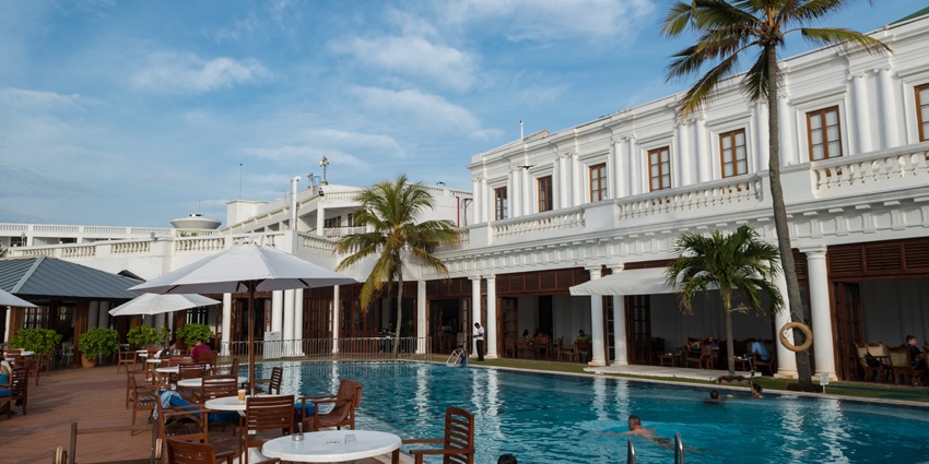 View of the beautiful building of Mount Lavinia Hotel with a swimming pool and palm trees.