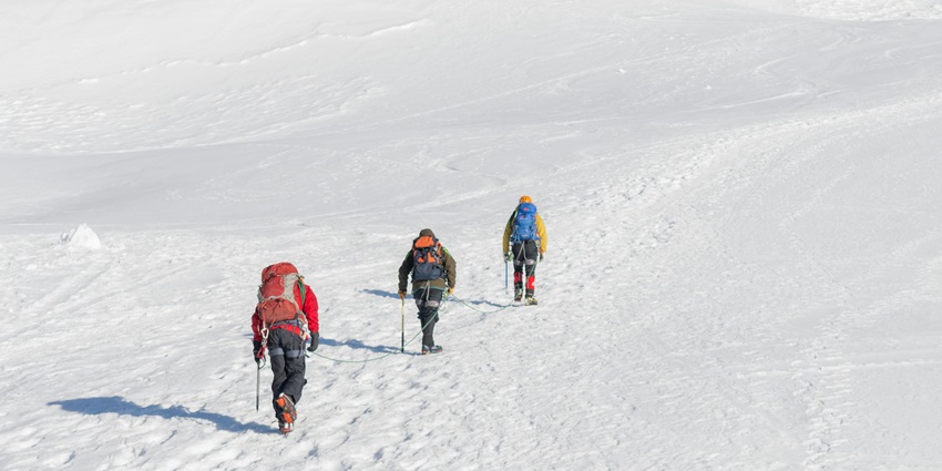 An enchanting view of three people climbing up a snowy mountain during the daytime.