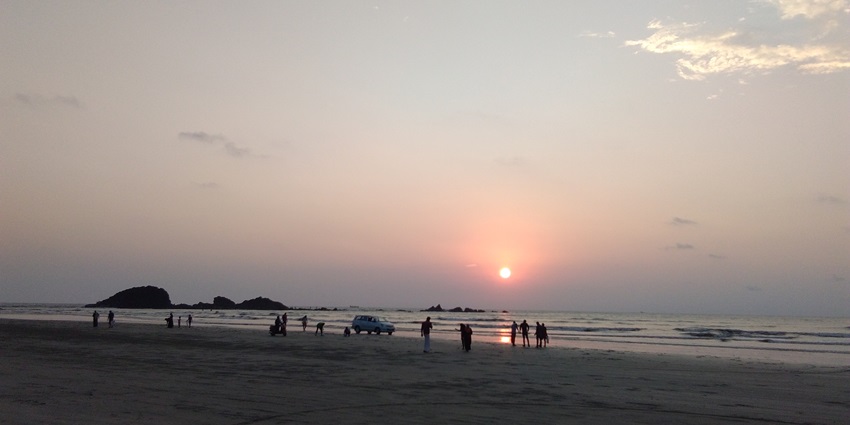 A picture of a beautiful sunset at a beach with a few visitors enjoying the twilight hour