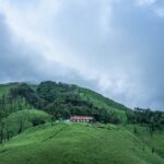 A stunning view of a lush green valley in Nagaland with a house on top during the day.