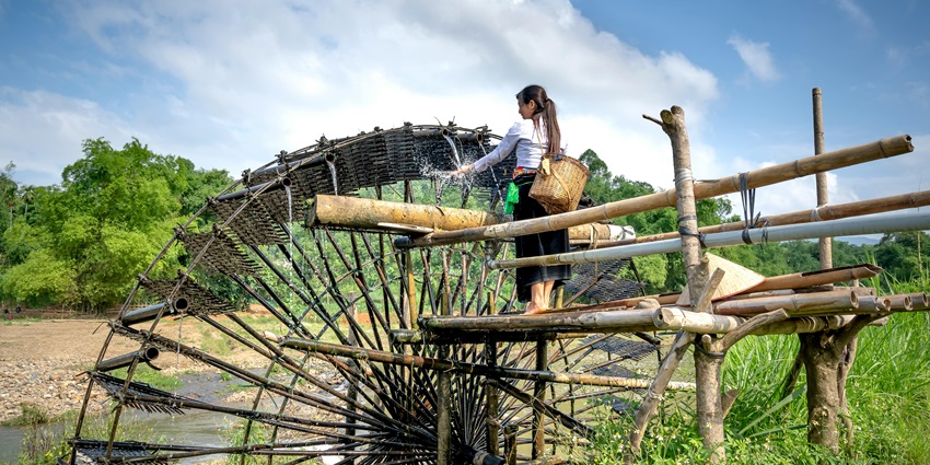 A picture of a bamboo water wheel with a woman washing hands from the wheel