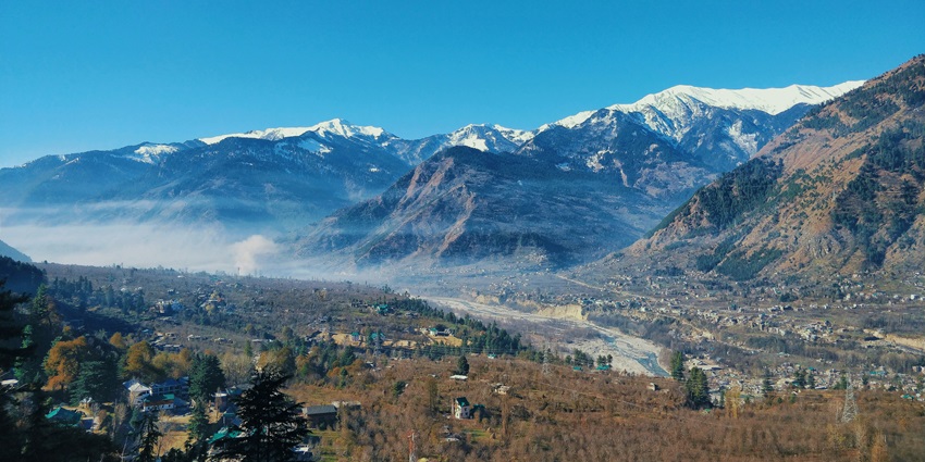 Image of picturesque Naggar Castle stands tall amidst lush green hills and a clear blue sky.