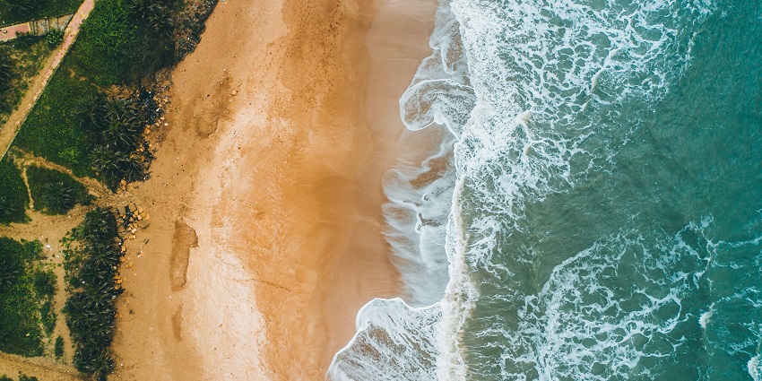 A beautiful aerial view of a beach with golden sands, turquoise waters, and lush verdure.