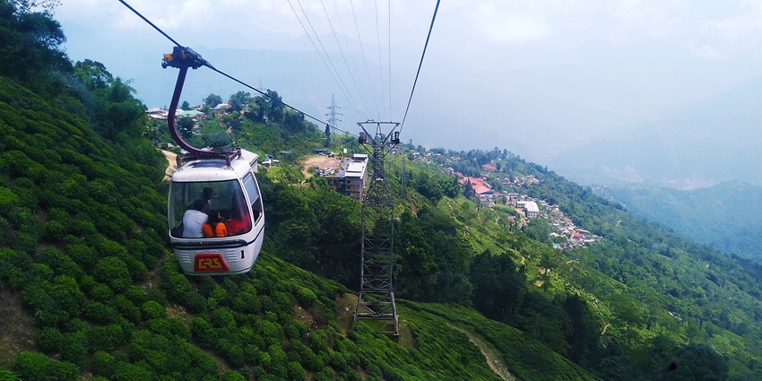 People sitting inside a cable-connected ropeway with mountains in the background