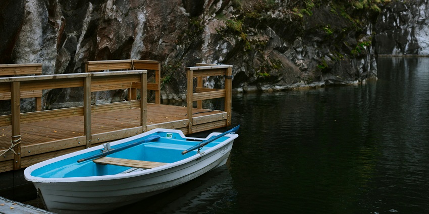 A captivating view of a small blue boat near a dock with a rocky mountain in the backdrop.