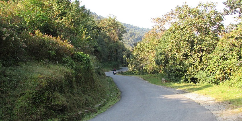 A road in Sikkim's hilly region with tall green mountains on the left side