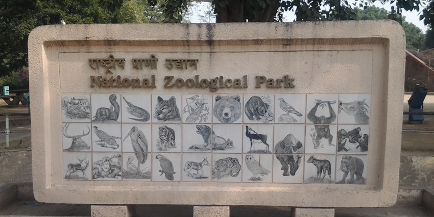 Delhi Zoo entrance gate with greenery, signage, and visitors walking through the area