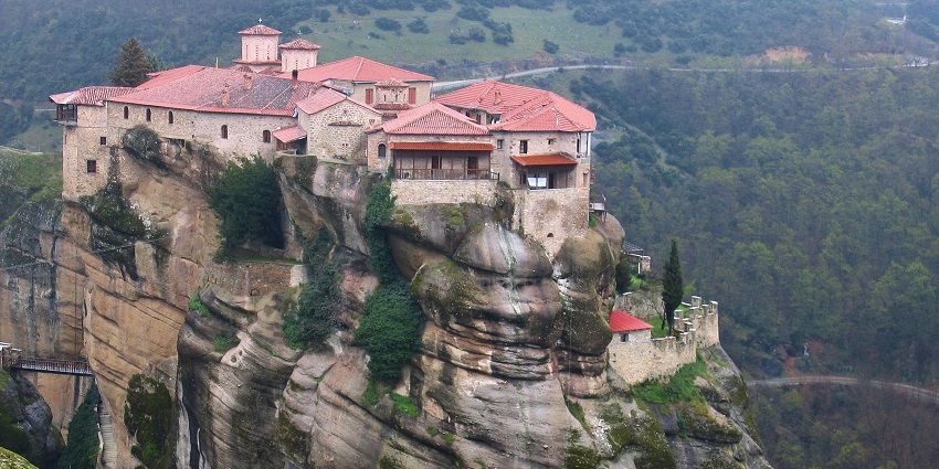 A picture of a monastery situated on a hill-top with scenic views of a mountain range in the background
