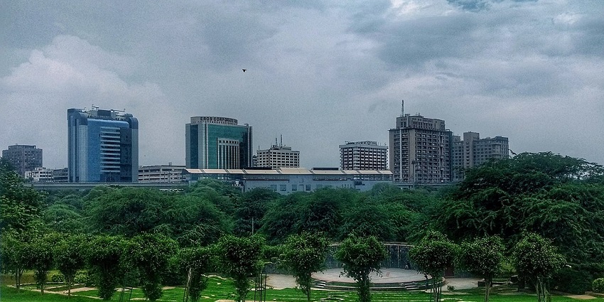 A picture of tall buildings in Delhi taken from a park with trees and greenery