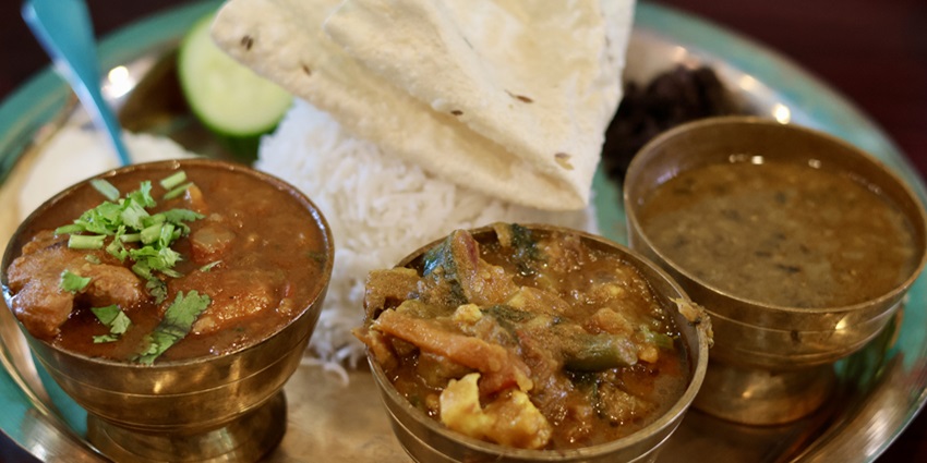 A traditional Nepali meal with rice, lentils, vegetables, meat, and pickles, served on a platter.