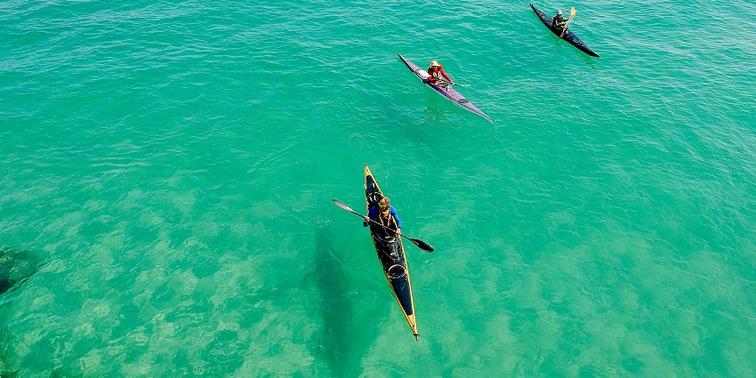 Three brightly colored yellow and pink kayaks lined up on the water, vibrant kayak options in Vietnam.