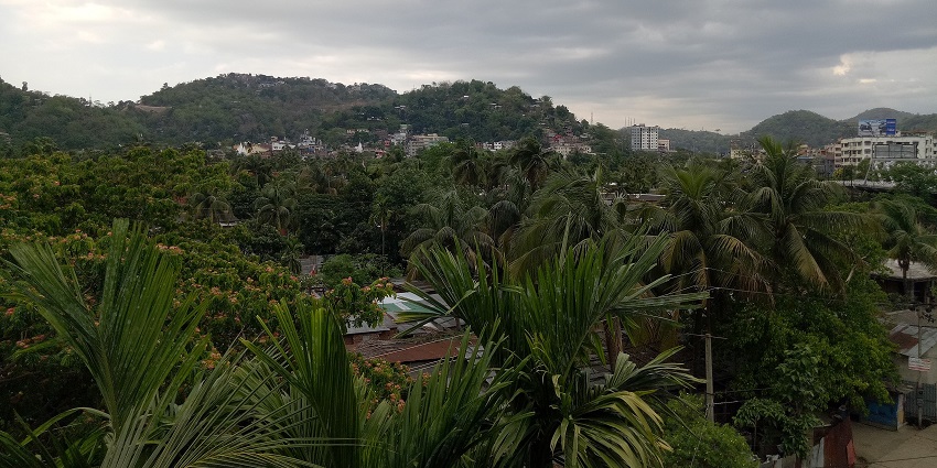 A picture of a lush green hill near Guwahati with a suburban settlement in the background