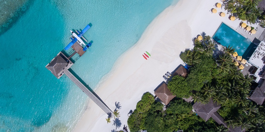 An aerial view of an island with trees and an aeroplane parked over the water nearby
