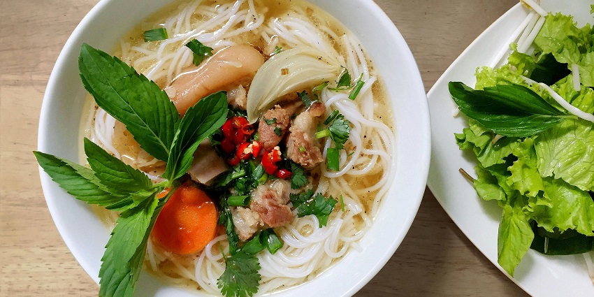 Image of deletable noodle bowl with veggies on and soup, on a white plate and bowl.