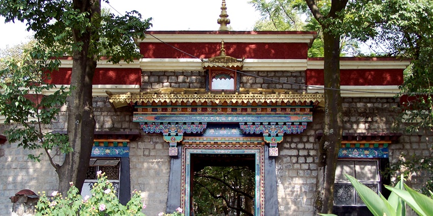 Ornate Tibetan-style gateway flanked by colorful pillars leading into serene garden paths.