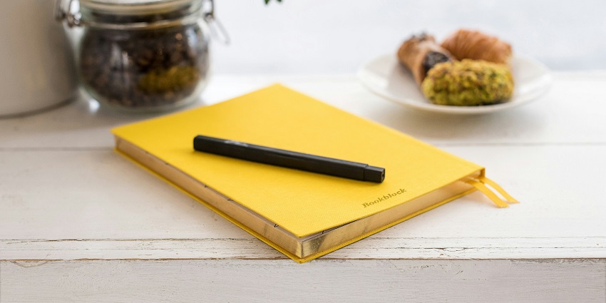 An image of a yellow binder notebook with a black pen over it kept on a white table.