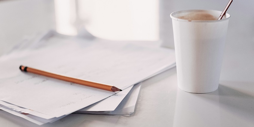 View of a pencil, multiple papers, and a disposable cup of coffee kept on a white table.