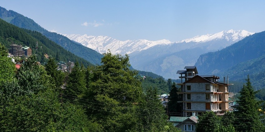 A picture of a green hill taken from close proximity, with snow mountains in the background