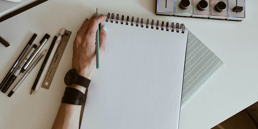 A picture of a notepad with plain pages and multiple stational kept on a white table.