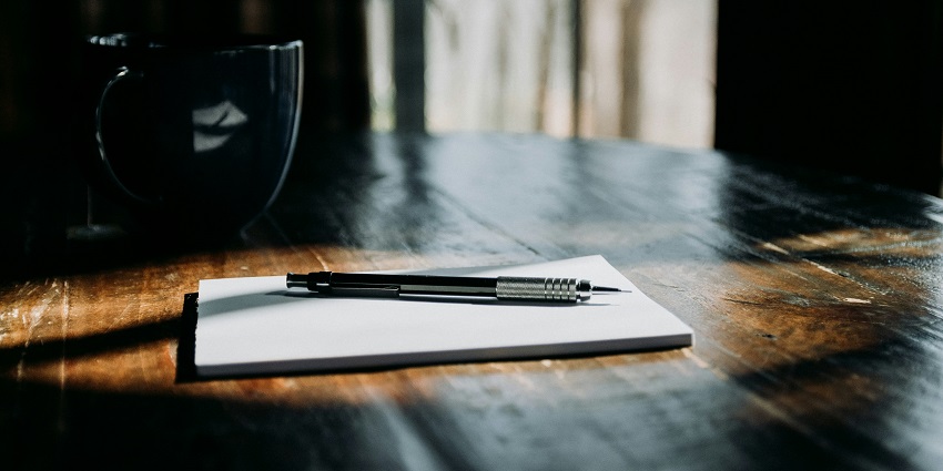 View of a pen kept on the top of a notebook, which is kept of a brown wooden table.