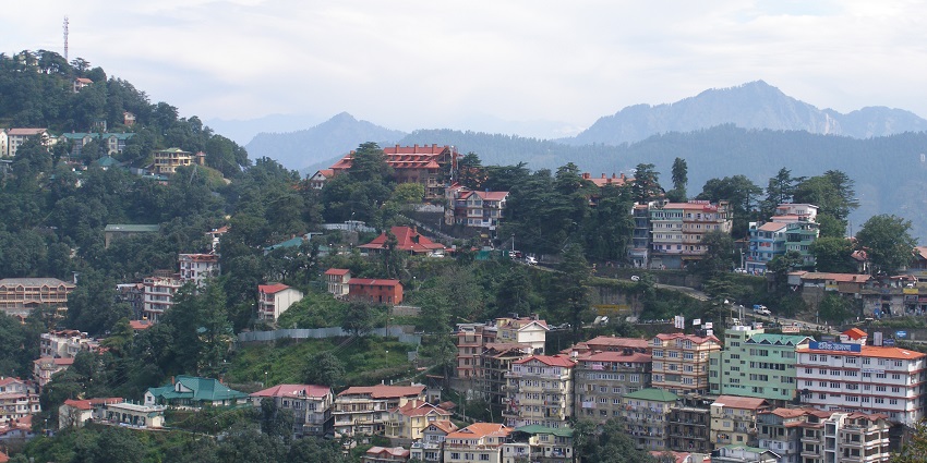 A distant view of a town in Himachal Pradesh with tall mountains in the background