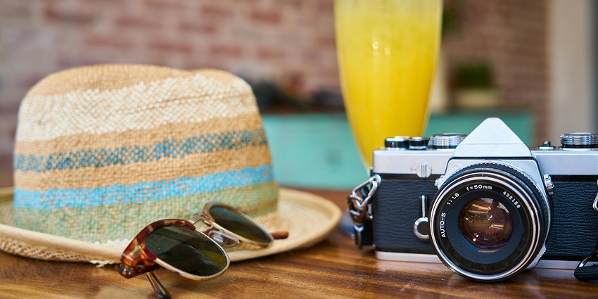 A grey and black DSLR camera, a sun hat and sunglasses - pack your travel essentials.
